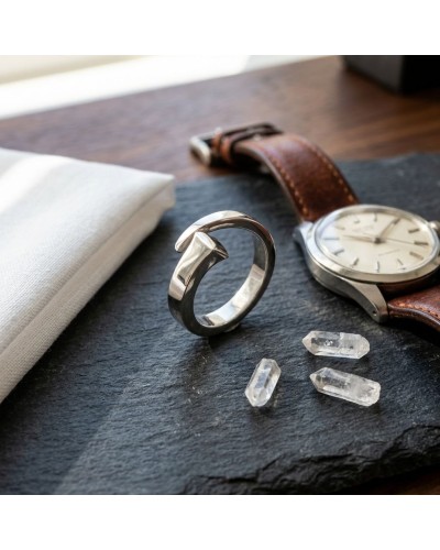 Bague CLOU homme en argent rhodié, près d’une montre à cuir et de petits cristaux sur une plaque sombre.
