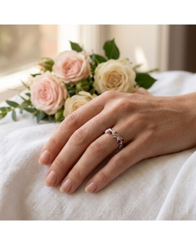 Alliance LAURIER femme en or: doigt féminin portant une bague argentée ornée de gemmes rouges, avec bouquet de roses pastel en a