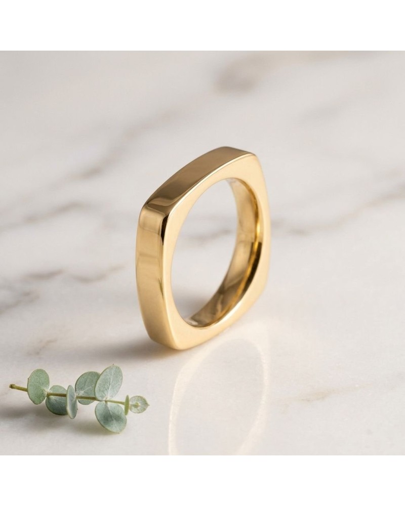 Alliance de forme carrée pour homme en or, bague épurée et brillante posée sur marbre avec brin de eucalyptus.