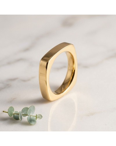 Alliance de forme carrée pour homme en or, bague épurée et brillante posée sur marbre avec brin de eucalyptus.