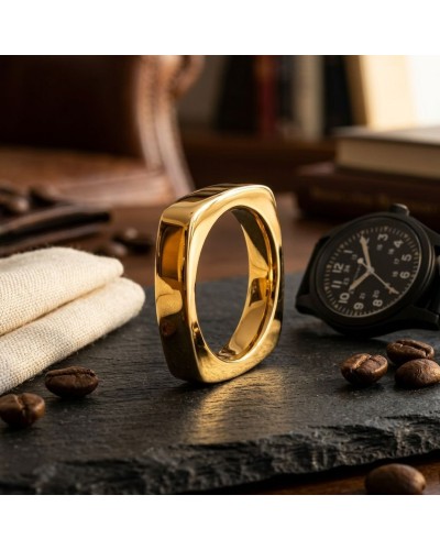 Alliance de forme carrée pour homme en or brillant posé sur une table avec montre militaire noire et grains de café, ambiance lu