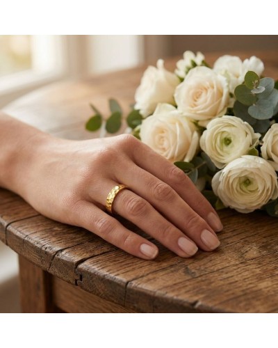 Alliance demi-martelée femme en or sur une main feminine, près d’un bouquet de roses crème sur une table en bois.