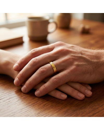 Alliance demi-martelée homme en or sur doigt, mains entrelacées sur une table en bois (focus sur la bague).