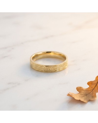 Alliance effet bois femme en or: bracelet en or jaune avec motif gravé, posé sur surface claire avec feuille d’automne.