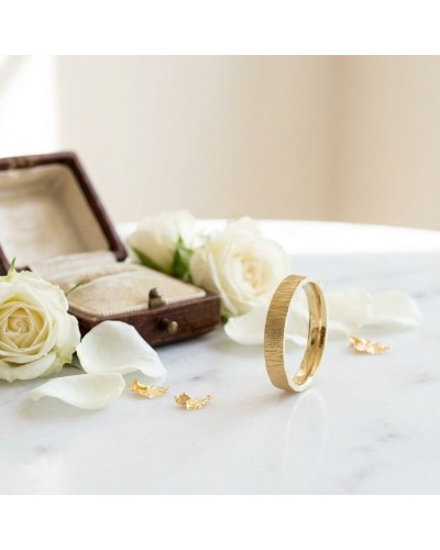 Alliance effet givré femme en or: bague dorée simple posée sur une surface, entourée de roses blanches et d’un petit écrin ouver