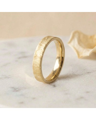 Alliance effet givré femme en or - bague dorée texturée, anneau simple posé sur une surface claire avec une petite fleur en arri