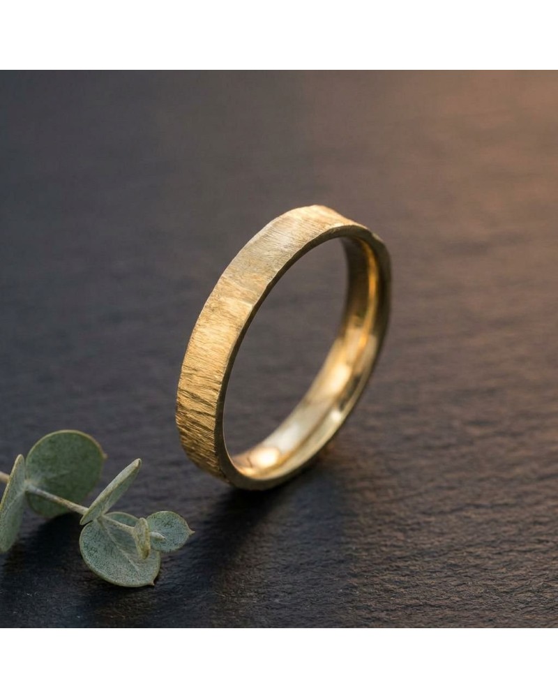 Alliance effet givré homme en or: bague masculine dorée au fini texturé, posée sur une surface sombre, avec une petite plante à