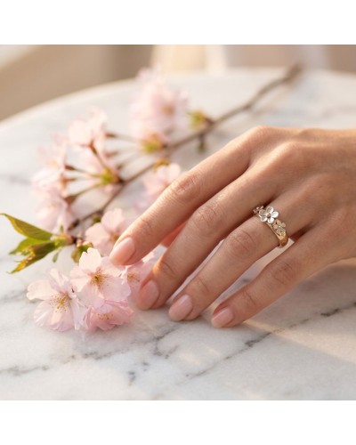 Bague CERISIER en or avec fleurs émaillées blanches sur doigt féminin, fleurs de cerisier roses à côté.
