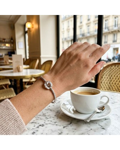Bracelet ouvrant en argent mat et brillant rhodié, serti de 6 oxydes blancs, worn on a wrist resting at a café table.