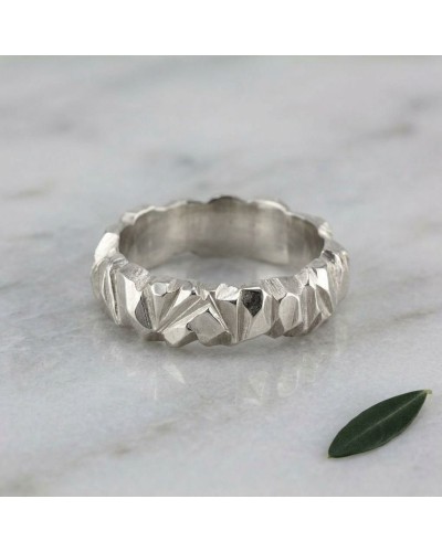 Alliance homme en argent brossé avec motif géométrique angulaire, bague texturée sur une surface claire avec une petite feuille