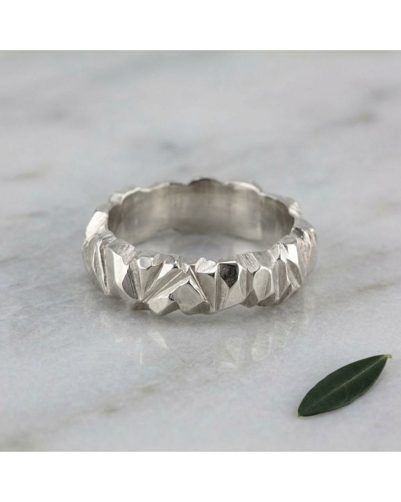 Alliance homme en argent brossé avec motif géométrique angulaire, bague texturée sur une surface claire avec une petite feuille