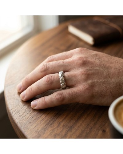 Alliance homme porte une bague argentée texturée sur le doigt, posé sur une table en bois près d’un livre. main masculine. ALLIA