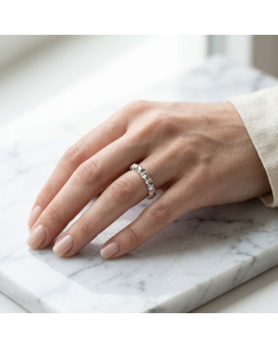 Alliances féminines : bague argentée à motif sculpté portée sur doigt, sur une surface marbrée.
