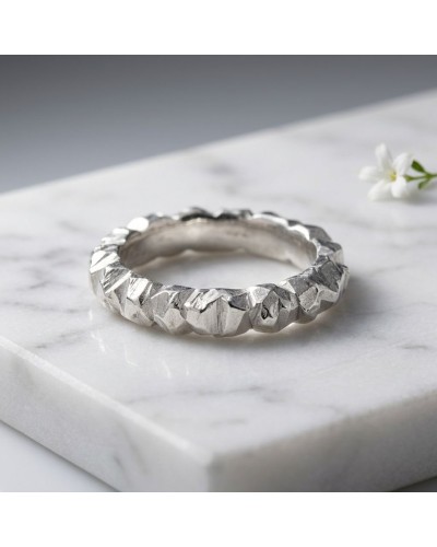 Alliance Marrow Femme: bague argentée à motif géométrique texturé, posée sur un marbre blanc, petit bouton floral en arrière-pla