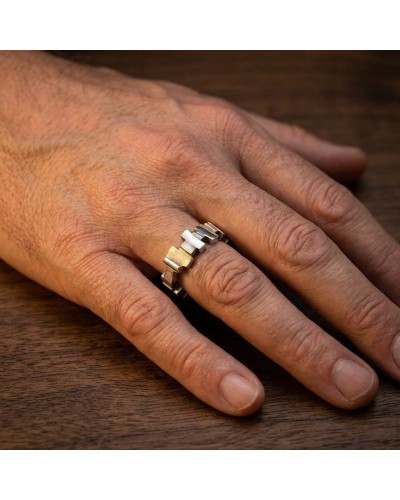 Alliance bicolore sur doigt masculin, bague à maillons carrés, or et argent, posé sur plan en bois.