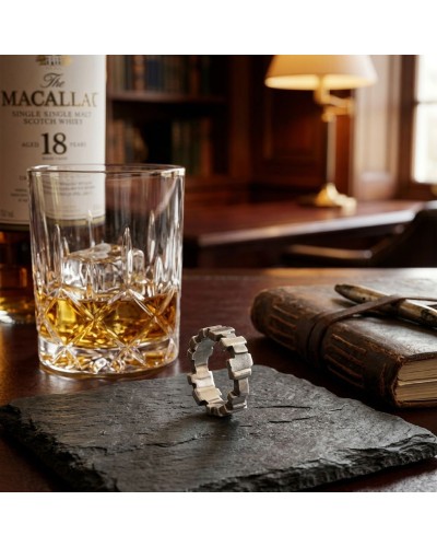 ALLIANCE BLADE HOMME: verre à whisky avec glaçons sur une nappe; flacon de Macallan en arrière-plan, pierre noire et livre ancie