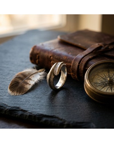 Alliage homme: chevalière argentée posée près d’une plume et d’une boussole antique sur une surface sombre, avec un vieux carnet