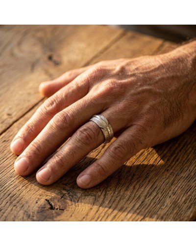 Anse rasée et doigt portant une bague argentée à motif géométrique sur table en bois. ALLIANCE GERONIMO HOMME.
