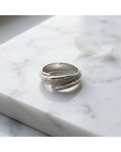 Alliances Poachontas Femme: bague argentée à motif enchevêtré feuilleté posé sur une surface marbrée, avec une plume blanche à c