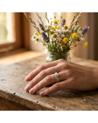 Anneau argenté posé sur le dos d’une main féminine sur une table en bois, bouquet de fleurs des champs en arrière-plan. Alllianc