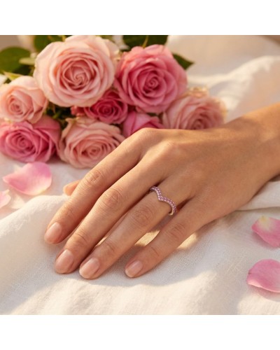 Alliance TIANA femme en or: une main féminine porte une bague serpentée pavée de pierres roses, sur fond de roses roses et pétal