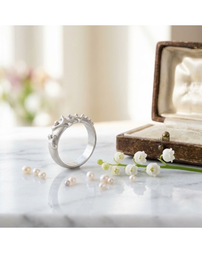 Alliance GRENOUILLE femme en or: bague argentée au motif animal stylisé, posée près d’un vieux coffret et de perles sur marbre.