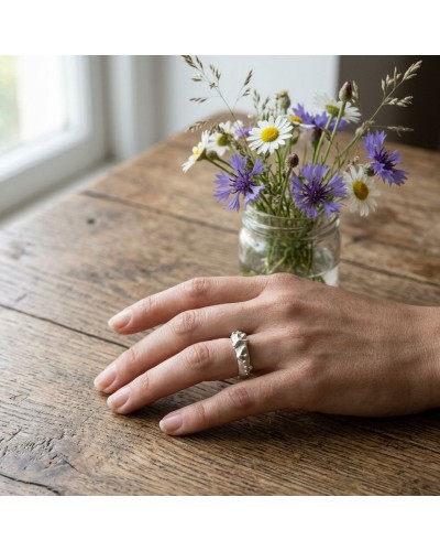 Alliance GRENOUILLE femme en or: une bague argentée sur le doigt de la femme, bouquet de fleurs sauvages dans un bocal en arrièr