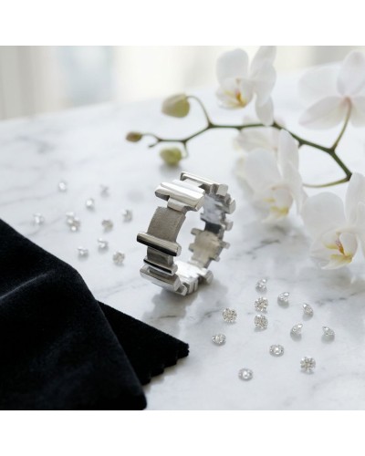 Anneau argenté géométrique posé sur marbre, entouré de diamants et de fleurs blanches, évoquant Alliance Blade Femme.