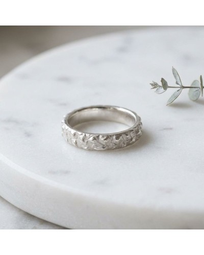 Alliance RHINOCÉROS homme en or: bague argentée à motif torsadé posée sur une surface blanche avec une petite branche verte en a