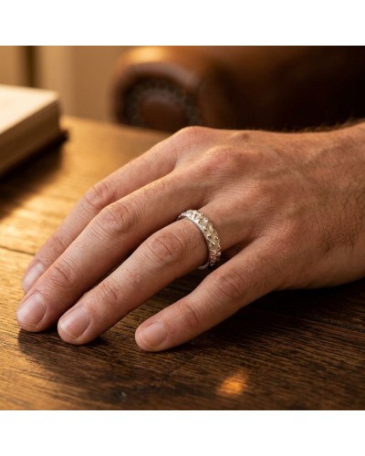 Alliance RHINOCÉROS homme en or: doigt masculin portant une bague argentée/acier gravée à motif bosselé sur table en bois.