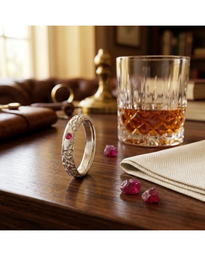 Alliance BISON homme en or : bague argentée texturée avec pierre rose, posé sur une table en bois près d’un verre à whisky et pi