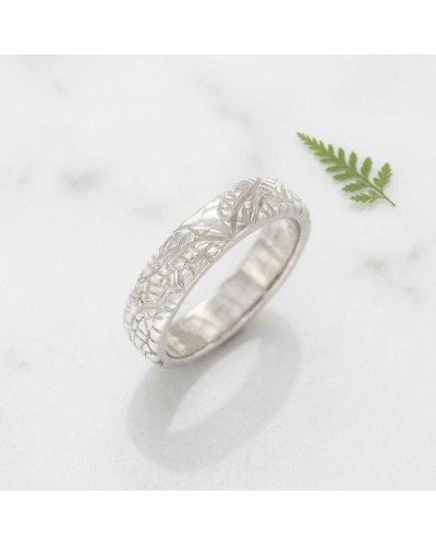 Alliance LIBELLULE femme en or: bague argentée ornée d’un motif floral délicat, sur fond marbré avec une petite feuille verte.