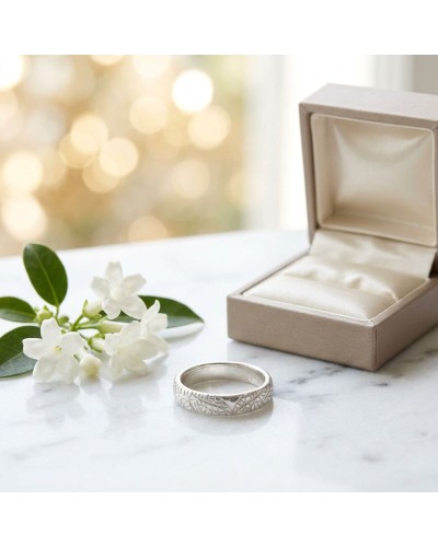 Alliance LIBELLULE femme en or: bague argentée gravée près d’un écrin beige sur marbre, fleurs blanches en arrière-plan.