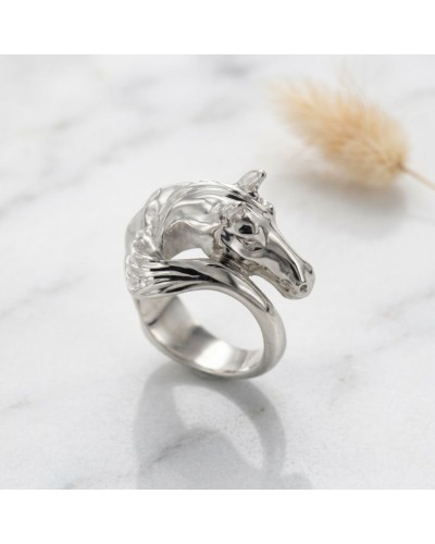 Bague argentée en forme de tête de cheval, détail brillant et sculpté sur anneau lisse, posé sur surface claire avec brin d’herb