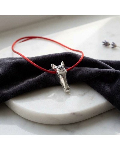 Pendentif en forme de cheval portant sur un cordon rouge, posé sur un drapé noir. QUÉROL.