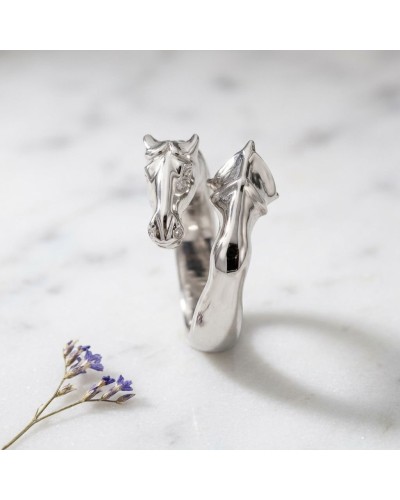 Bague ROCCIO en argent façon tête de cheval stylisée, sculptée et brillante sur fond clair avec fleur violette au premier plan.