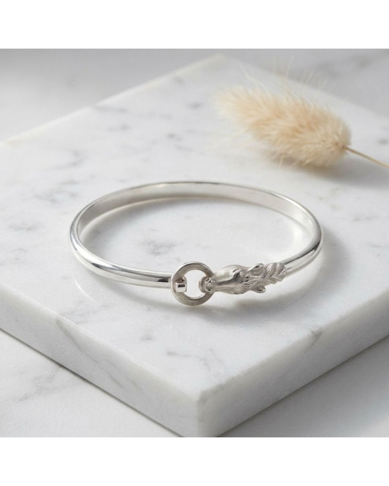 Bracelet en argent mat et brillant rhodié, motif plume avec petit cercle, posé sur une plaque marbrée.