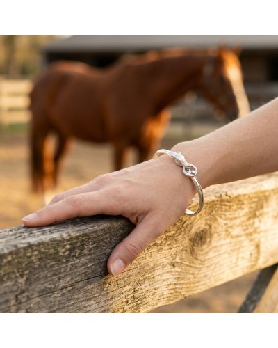 Bracelet en argent mat et brillant rhodié autour du poignet, posé sur une barrière en bois avec cheval au fond.