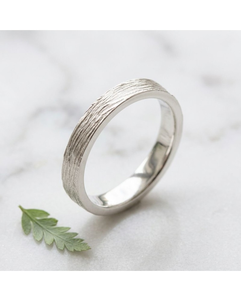 Alliance NERVURE 4 mm Homme en or: bague élégante argentée à texture nervurée sur fond clair, près d’une feuille verte.