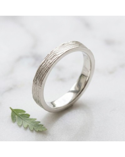 Alliance NERVURE 4 mm Homme en or: bague élégante argentée à texture nervurée sur fond clair, près d’une feuille verte.
