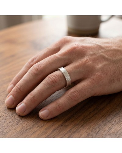 Alliance NERVURE 4 mm Homme en or : close-up sur doigt avec bague argentée texturée, sur table en bois.