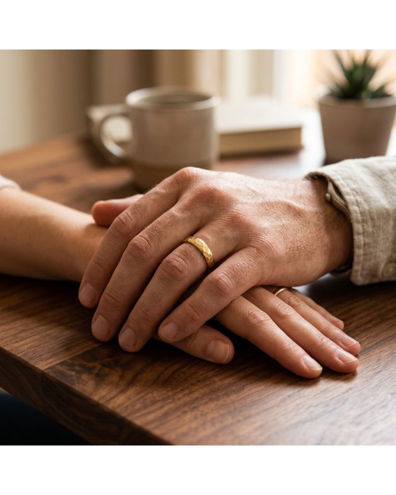 Alliance homme en or bombée avec un effet martelé sur une table, mains jointes et bague visible.