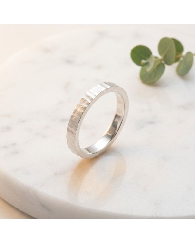 Alliance BASALTE 4 mm Femme en or: bague argentée à texture martelée reposant sur une surface claire avec brins de eucalyptus en