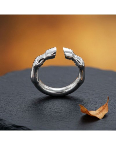 Bague TROT homme en argent rhodié, ouverte et sculptée, posée sur une surface sombre avec une feuille orange au premier plan.