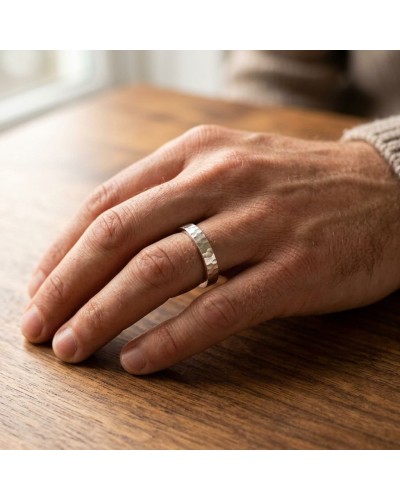 Alliance BASALTE 4 mm Homme en or: doigt portant une bague argentée texturée sur une main masculine reposant sur une table en bo