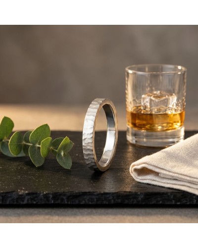 Alliance BASALTE 4 mm Homme en or: bague en métal texturé posée sur une plaque, verre à whisky et ramequin à côté, branches de e
