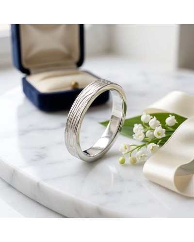 Alliance NERVURE 4 mm Femme en or: bague argentée texturée près d’un bouquet de petites fleurs et d’un écrin bleu.