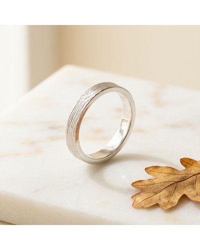 Alliance NERVURE 4 mm femme en or: bague argentée à texture nervurée posée sur une surface claire, feuille d’automne à côté.
