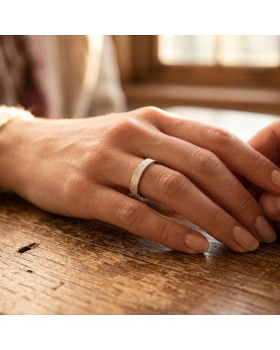 Alliance NERVURE 4 mm Femme en or: doigt féminin portant une bague argentée/ or pâle à bord plat sur une table en bois.