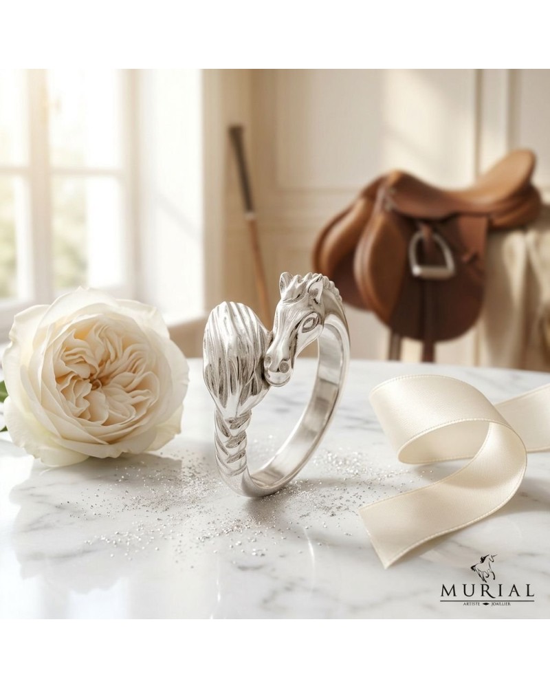 Bague argentée MIKA en forme de dragonne enroulée sur un doigt, avec voile satin et rose blanche en arrière-plan.